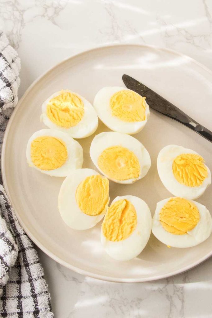 Air fryer hard boiled eggs in a ceramic plate with a black butter knife