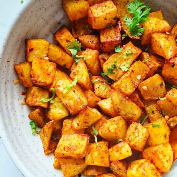 air fryer potato cubes in a white ceramic plate with black spoon