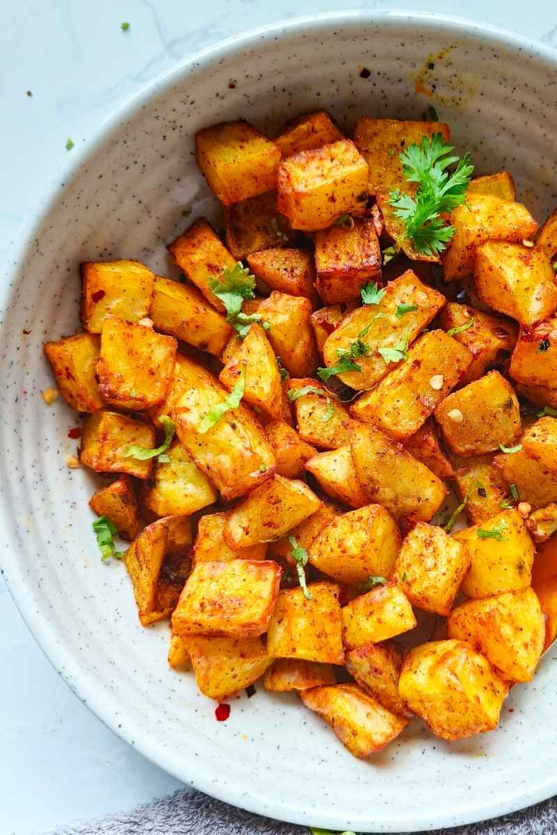 air fryer potato cubes in a white ceramic plate with black spoon