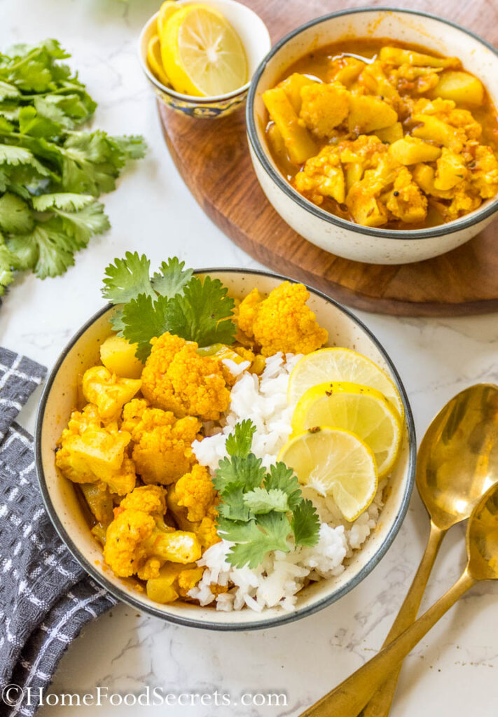 Close up of final vegan cauliflower chickpea curry served with rice, cilantro and slices of lime