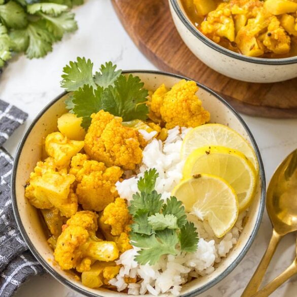 Close up of final vegan cauliflower chickpea curry served with rice, cilantro and slices of lime, golden spoon
