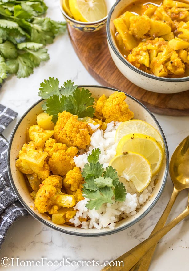 Close up of final vegan cauliflower chickpea curry served with rice, cilantro and slices of lime, golden spoon