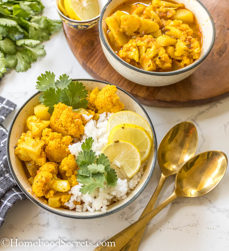 Close up of final vegan cauliflower chickpea curry served with rice, cilantro and slices of lime, golden spoons