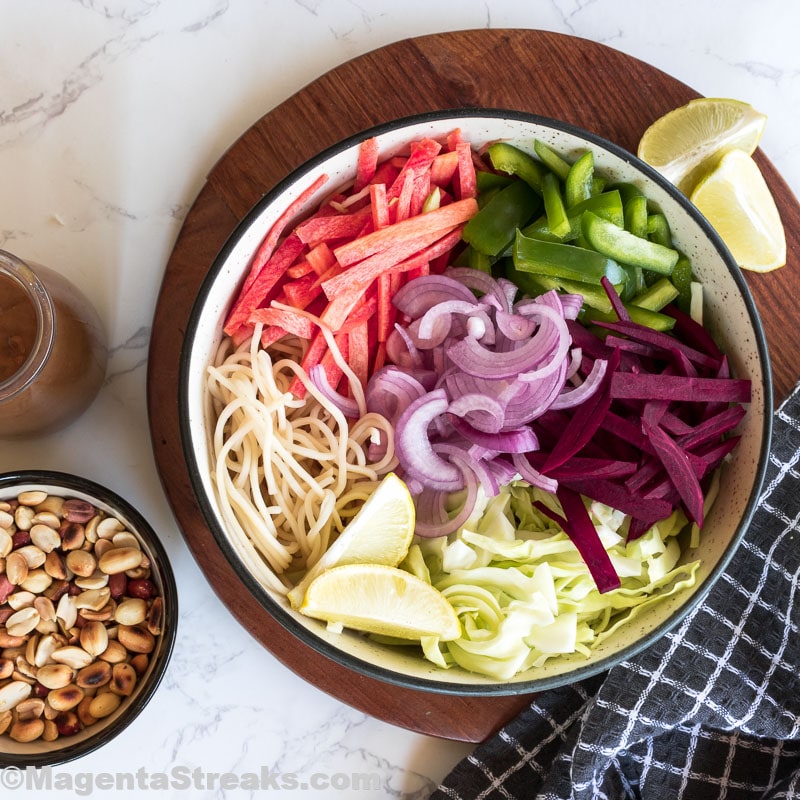 chopped veggies and cooked pasta in a white bowl with roasted peanuts and thai peanut sauce thai peanut pasta salad recipes-min