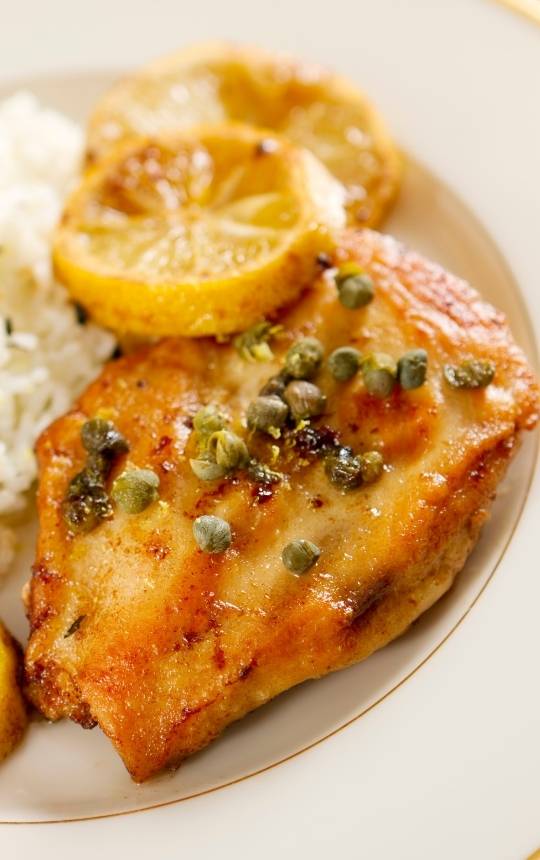 chicken piccata dish with rice and lemon wedges