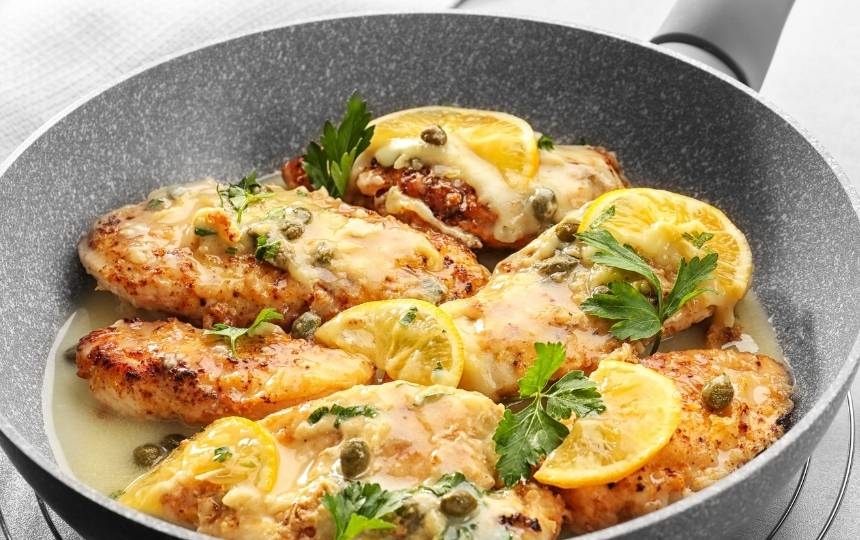 chicken piccata recipe in a pan with lemon wedges