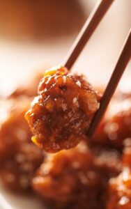close up to general tso's chicken piece with chopstick