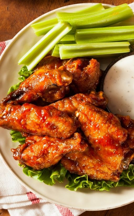 A pile of baked buffalo wings with celery sticks and ranch dressing