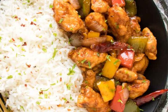 Szechuan Chicken recipe in a black plate with a golden and balck spoon alont with fresh cilantro and red bell pepper