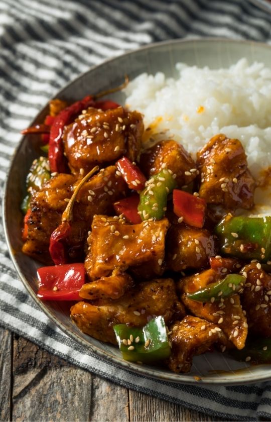 Szechuan chicken with vegetables and chili peppers in a plate over white rice