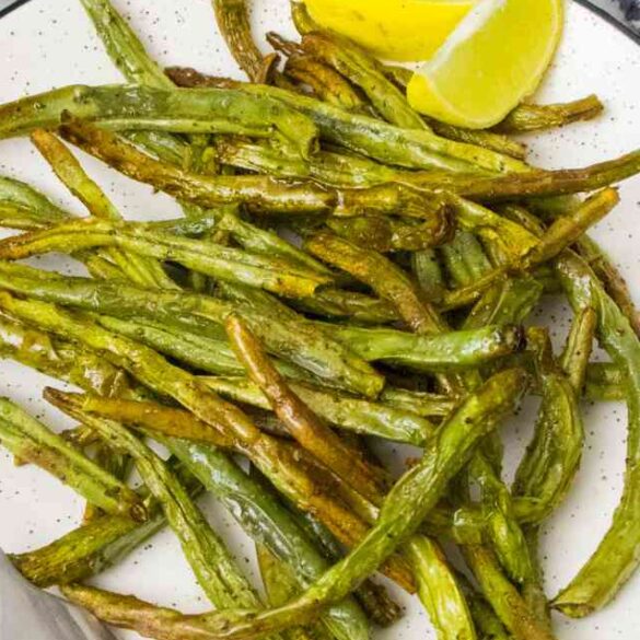 close up to air fryer green beans on a white plate with 2 lemon wedges