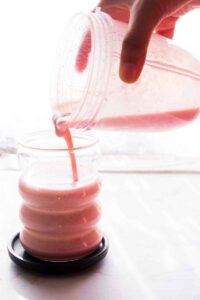 Strawberry banana smoothie being made in Vitamix blender and poured into glasses.