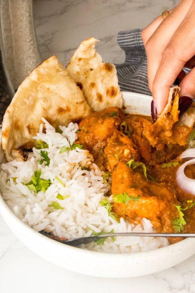 A bowl full of creamy chicken tikka masala over white basmati rice,and with a slice of butter naan.