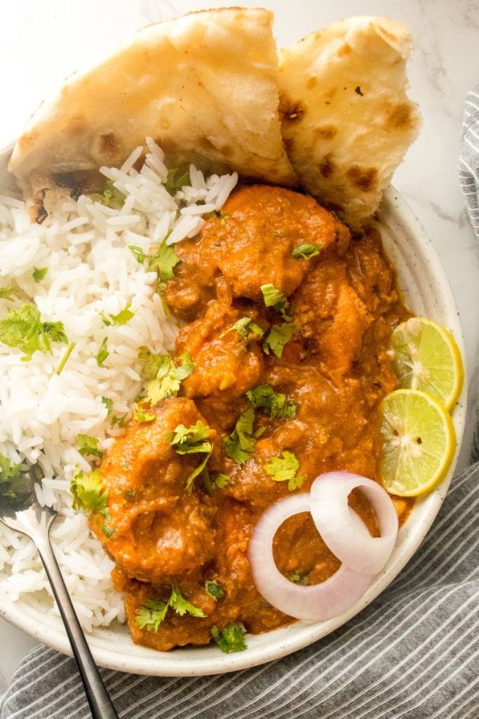 Chicken tikka masala in bowls with rice, butter naan, onion and lemon wedges