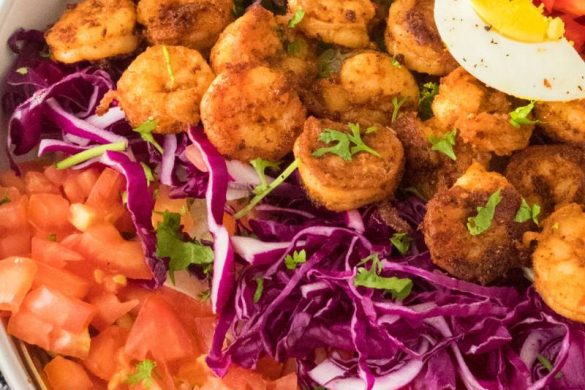 a large shrimp cobb salad with rows of shrimp, hard boiled eggs, chopped veggies, and fresh green onion on the top