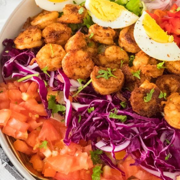 a large shrimp cobb salad with rows of shrimp, hard boiled eggs, chopped veggies, and fresh green onion on the top