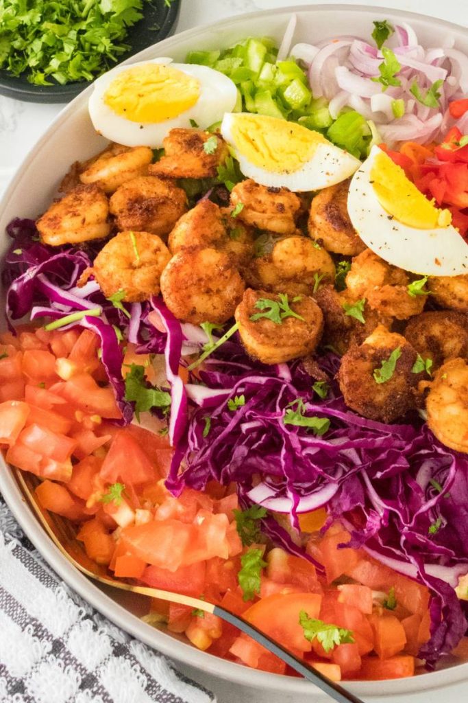 a large shrimp cobb salad with rows of shrimp, hard boiled eggs, chopped veggies, and fresh green onion on the top