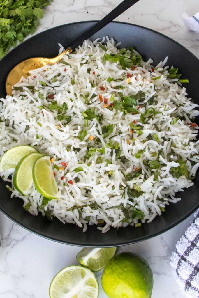 Black bowl of cilantro lime rice with chili flakes and lemon wedges.
