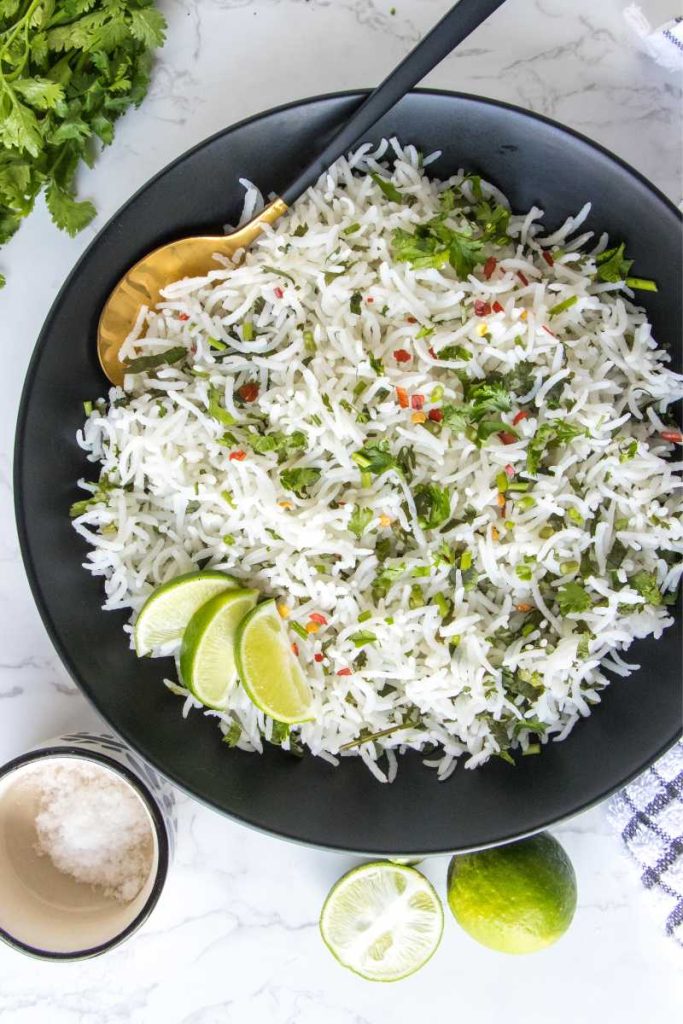 Cilantro lime rice in black bowl, garnished with chili flakes and lemon wedges.