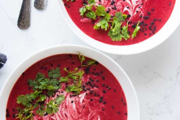 beet soup in a large white bowl garnish with white cream and chopped cilantro