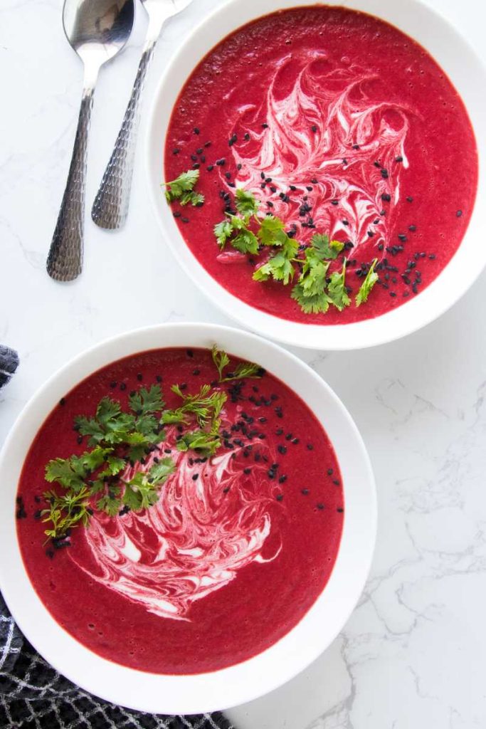 beet soup in a large white bowl garnish with white cream and chopped cilantro