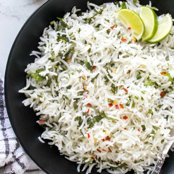 black bowl filled with cilantro lime rice, garnished with red chili flakes, and topped with lemon wedges