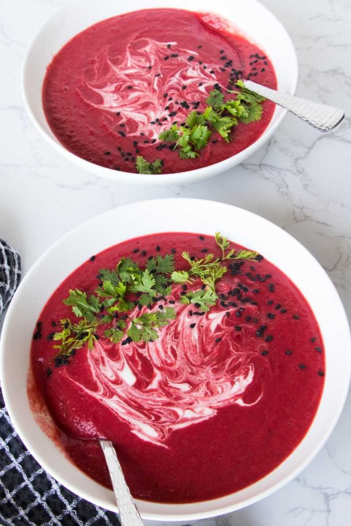 homemade beetroot soup in a large white bowl garnish with white cream and chopped cilantro