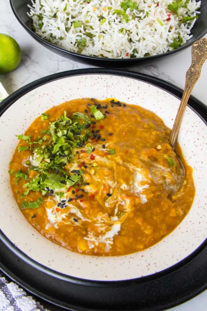 red lentil soup served on white bowl with fresh cilantro along with white rice