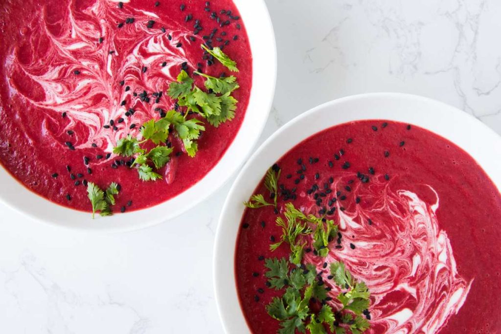 vegan beet soup in a large white bowl garnished with white cream and chopped cilantro