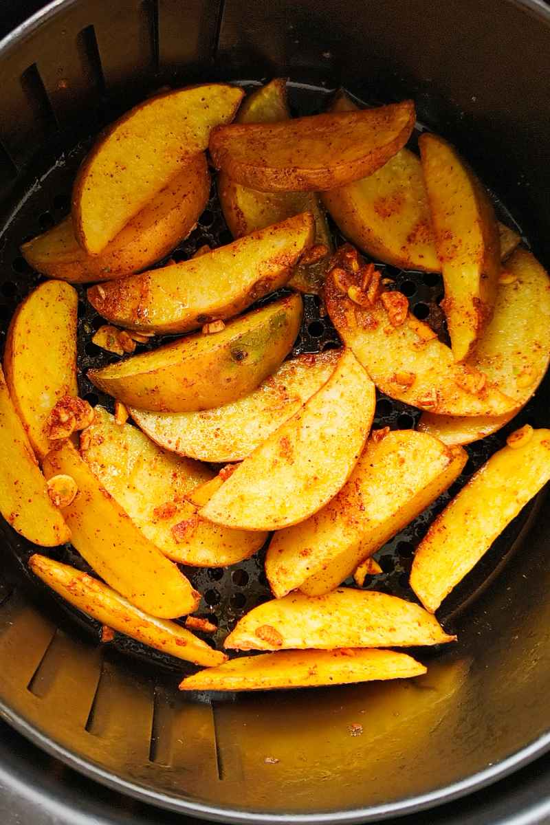 Air Fryer Potato Wedges uncooked in an air fryer basket with fresh chopped garlic