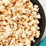 Popcorn in a black serving bowl piled high with a kitchen towel beside