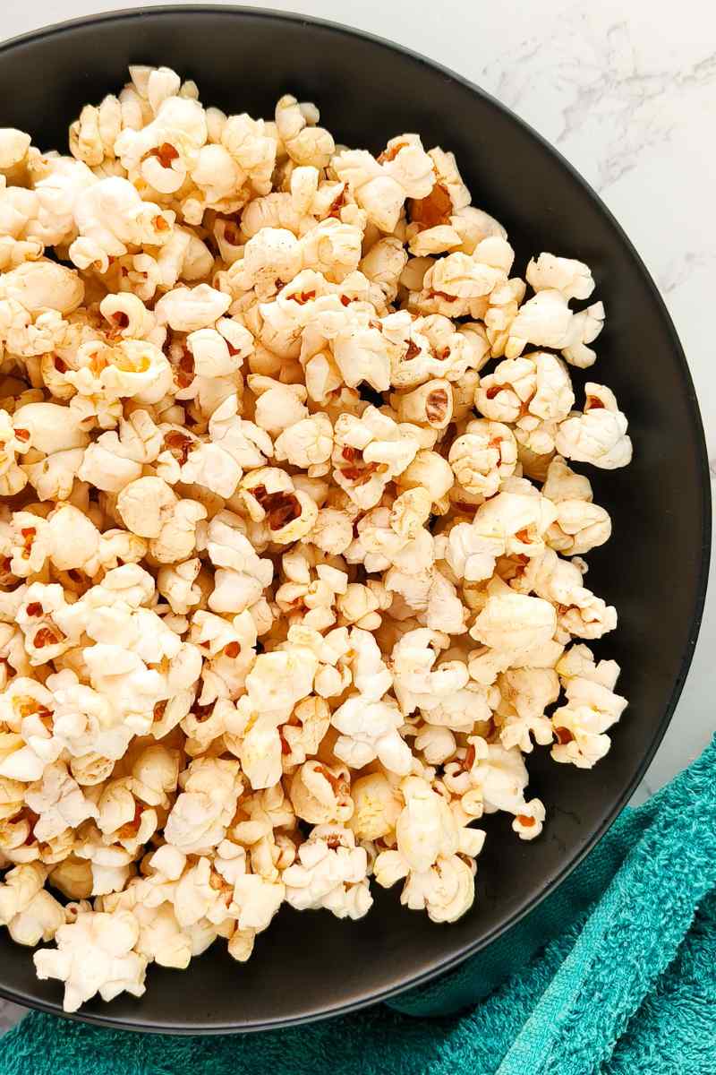 Popcorn in a black serving bowl piled high with a kitchen towel beside