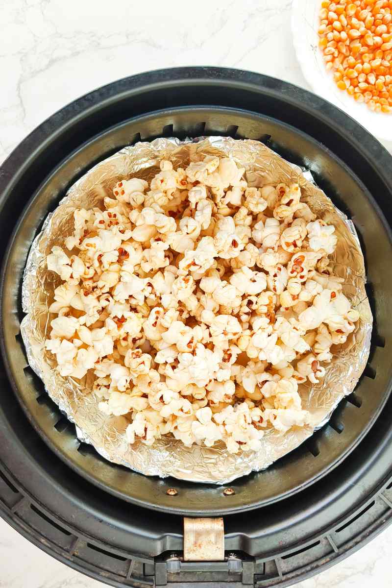 Popcorn in an air fryer basket lined with foil after cooked