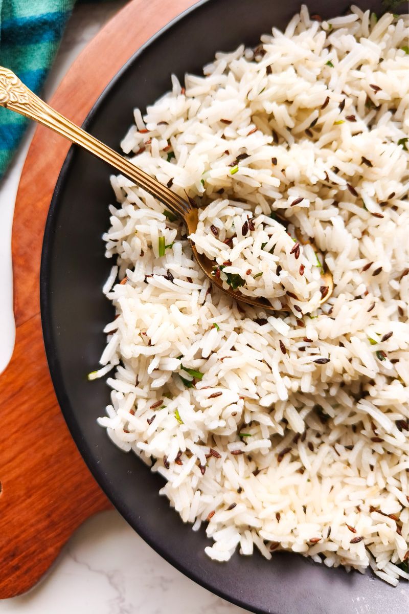 closeup of jeera rice in a black plate with golden spoon