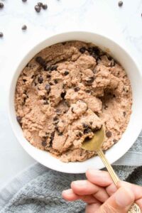 A golden spoon holding a spoon full of cottage cheese cookie dough over a bowl full of high protein dough