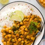 creamy coconut chickpea curry served in a white plate with white rice and lemon wedges