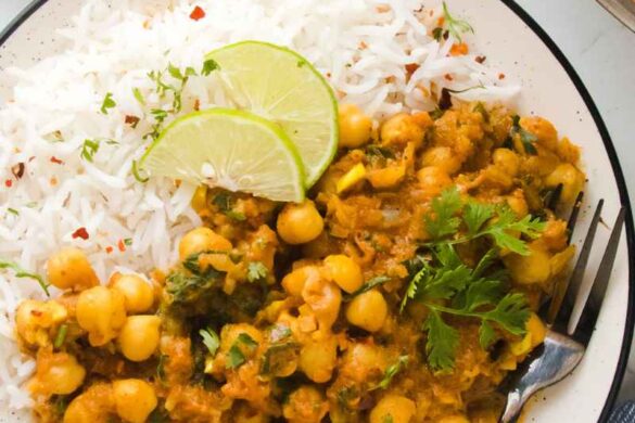 creamy coconut chickpea curry served in a white plate with white rice and lemon wedges