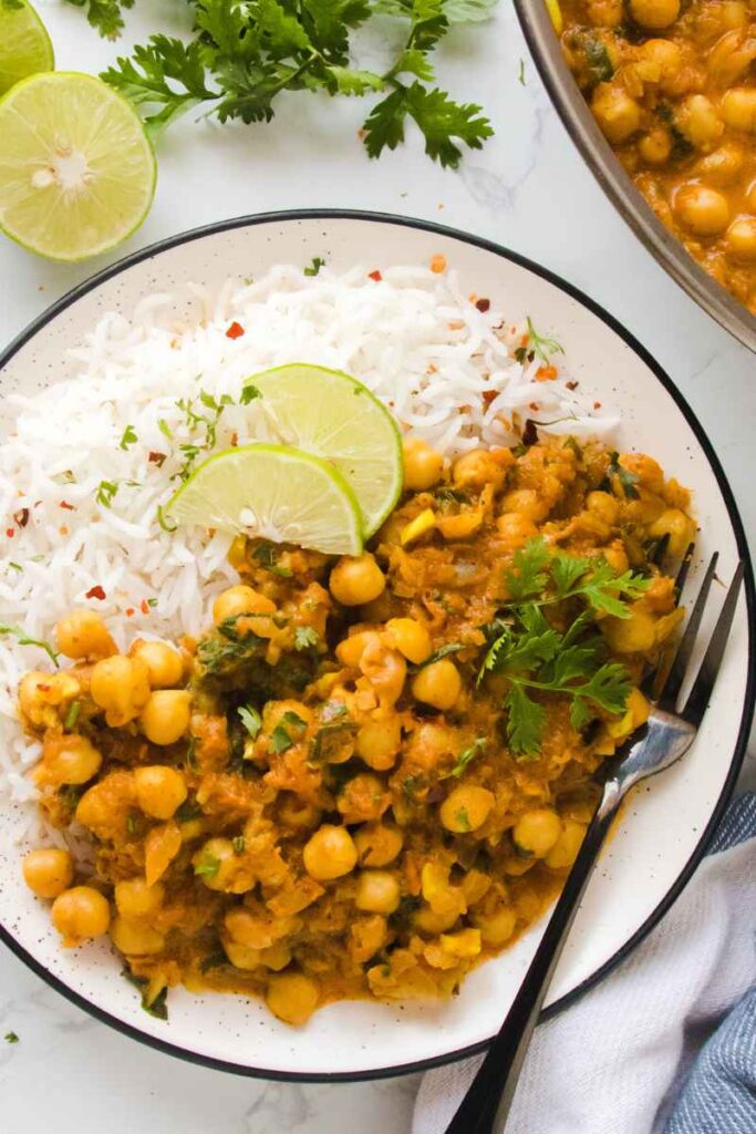 creamy coconut chickpea curry served in a white plate with white rice and lemon wedges