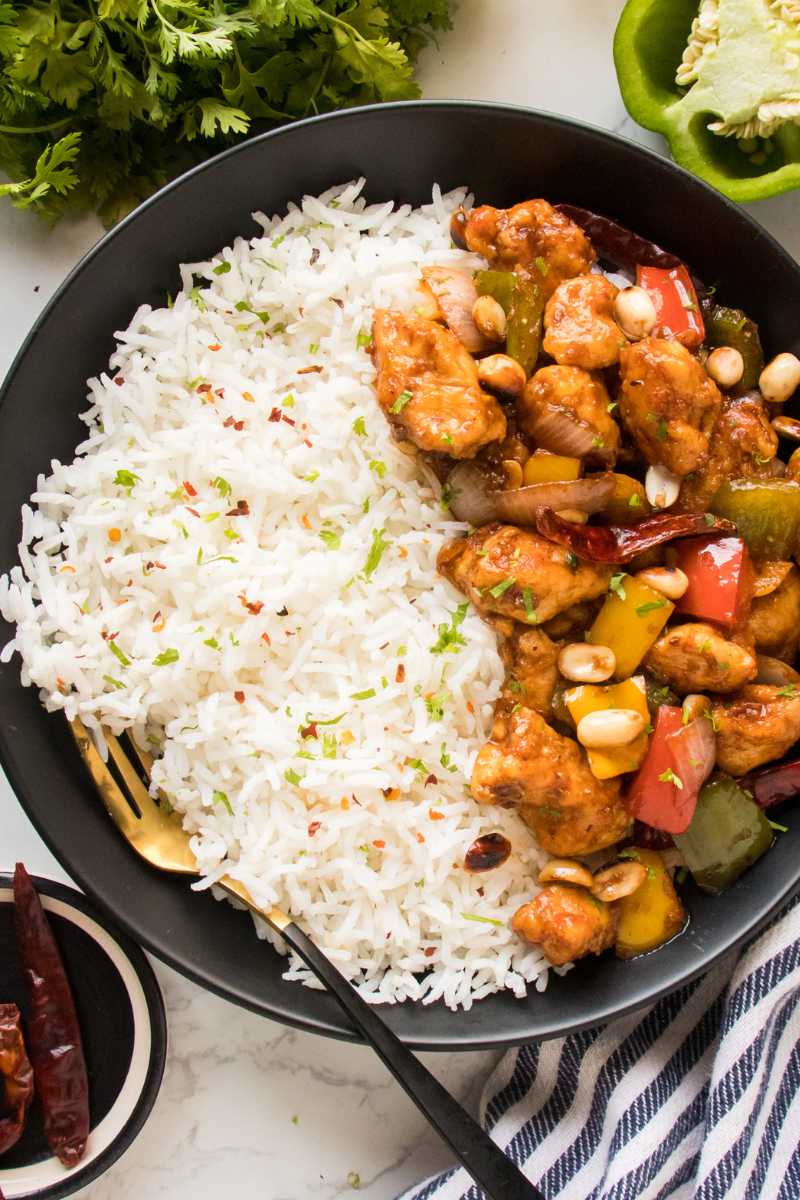 kung pao chicken recipe in a black bowl served with white rice garnished with cilantro