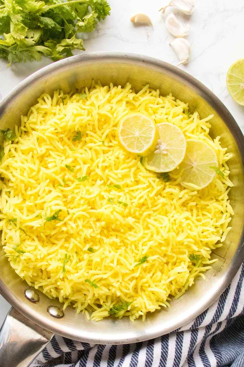 lemon rice with leom slices in stainless steel pan with cilantro and garlic cloves